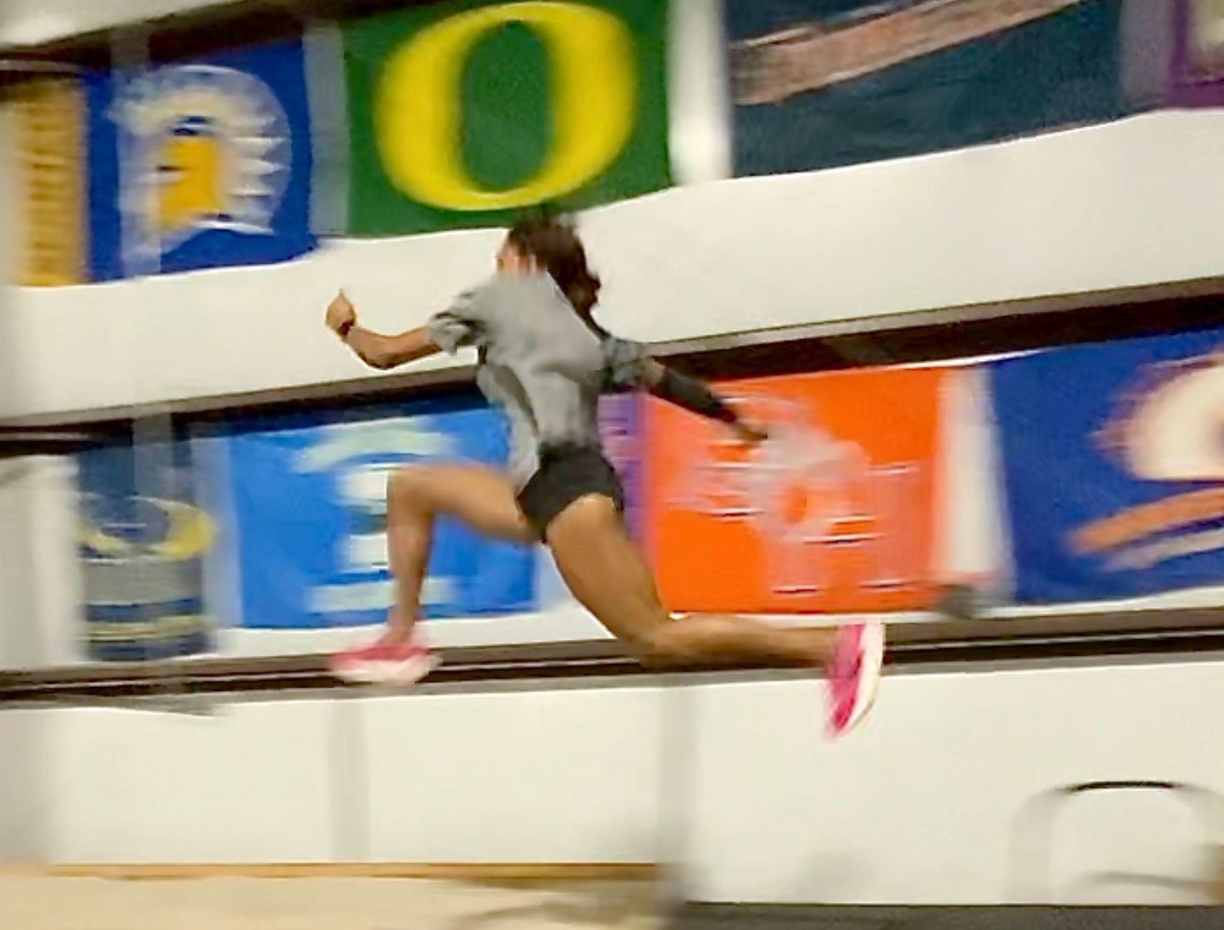 Athlete performing a jump indoors, with various banners hanging in the background.