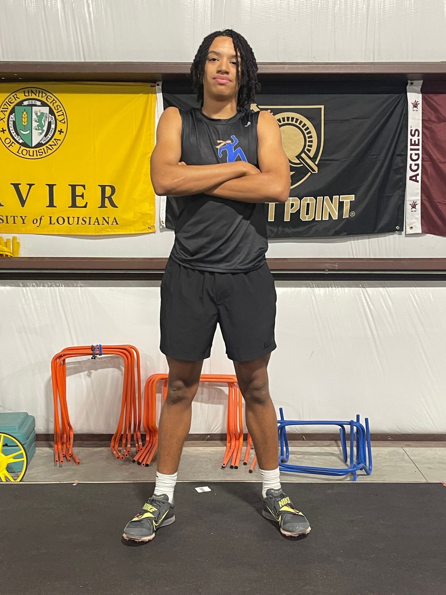 Athlete standing with arms crossed in front of sports banners and training hurdles.