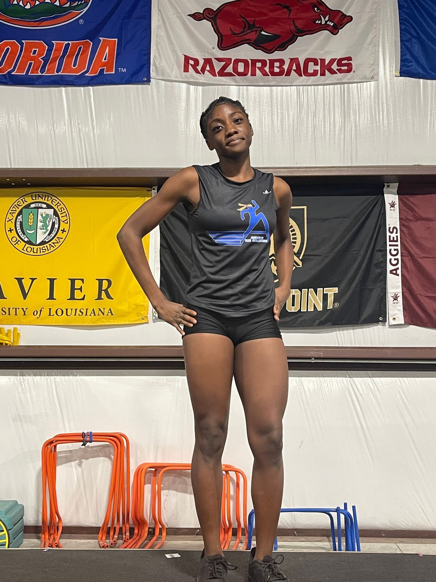 Athlete standing in a gym with university banners in the background, wearing sportswear and sneakers.