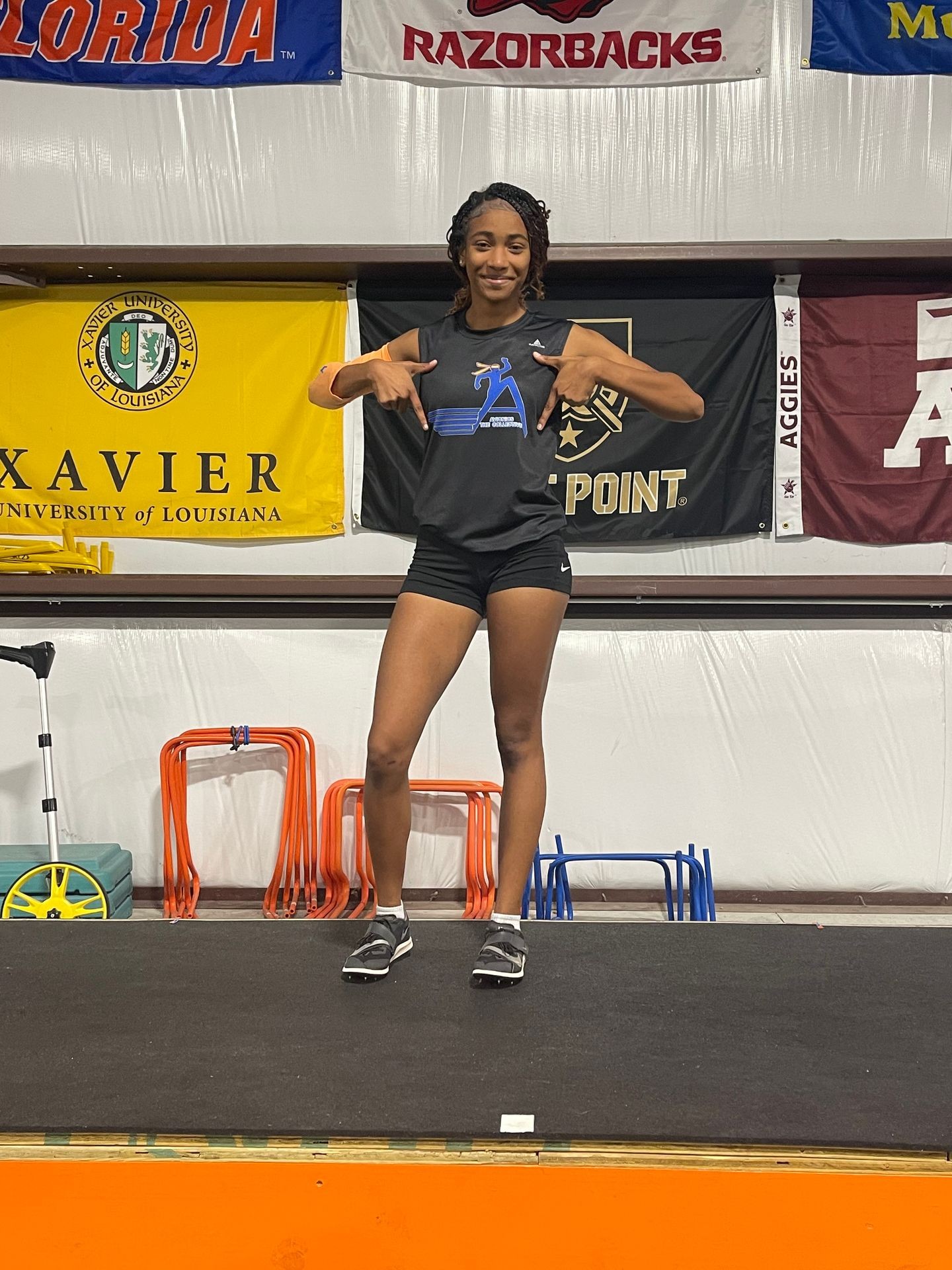 Smiling athlete in a black outfit posing on a mat, with sports banners in the background.