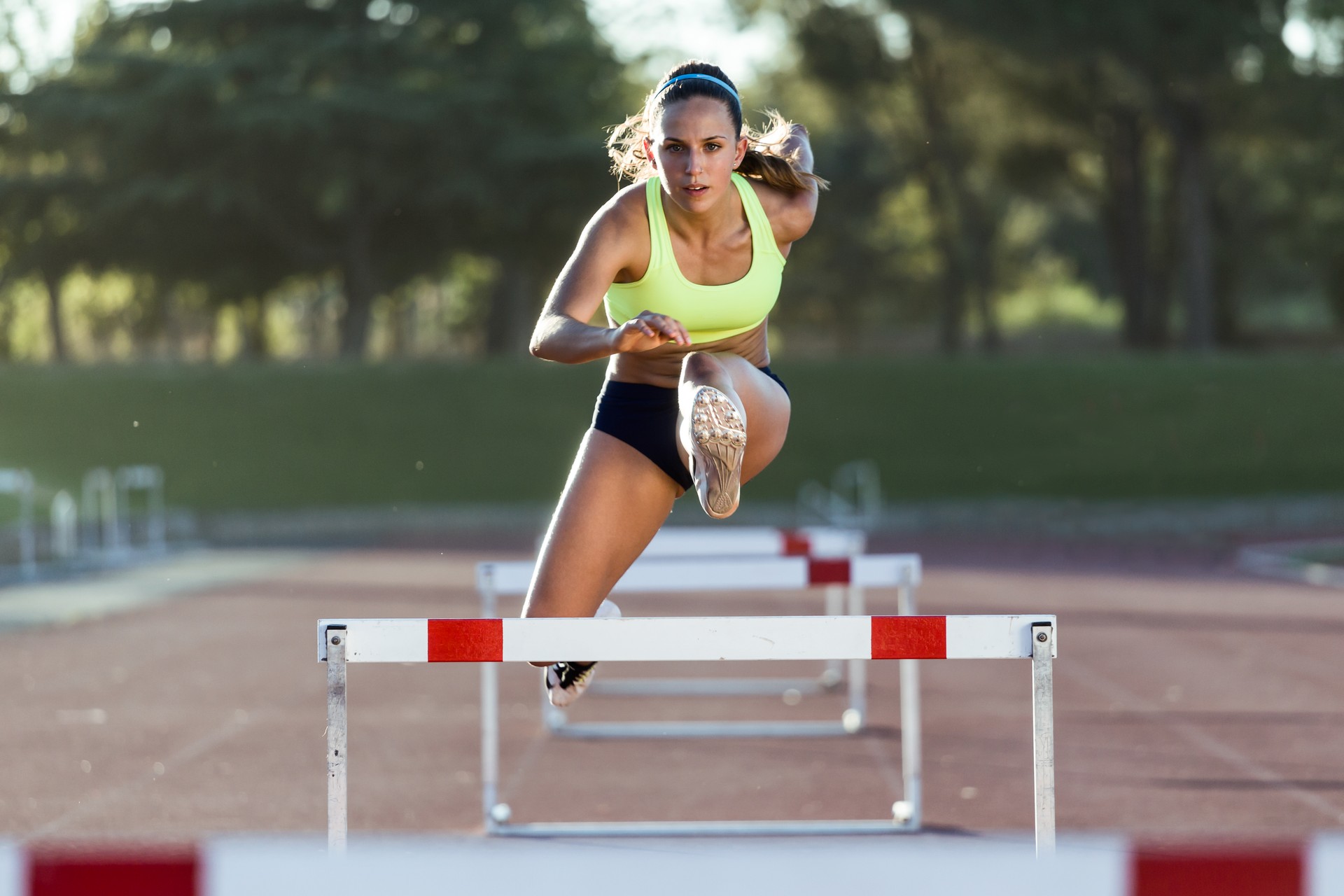 Young athlete jumping over a hurdle during training on race track.